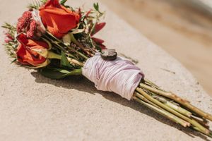 A beautiful red and pink floral bouquet wrapped in light pink ribbon lying on sand.