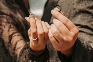 Close-up shot of hands wearing engagement rings against a natural backdrop.