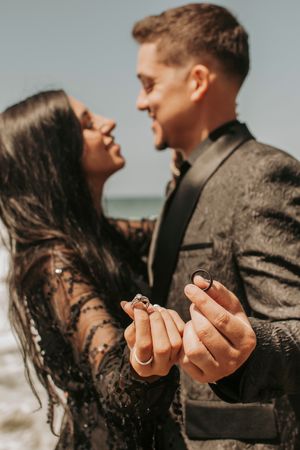 Couple sharing intimate moment on beach while showing engagement rings.