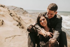 Happy couple embracing on coastal rocks during romantic photoshoot.