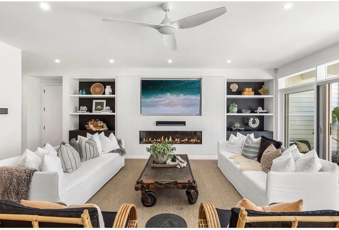 Modern coastal living room with fireplace, white sofas and ocean artwork.