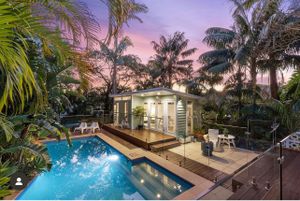 Tropical backyard with illuminated pool and palm trees at sunset.
