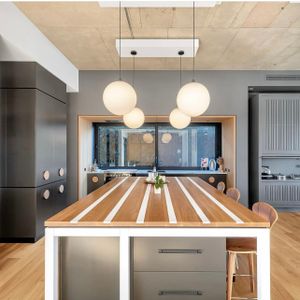 Modern kitchen with wooden countertop featuring white stripes and pendant globe lights hanging from wooden ceiling.