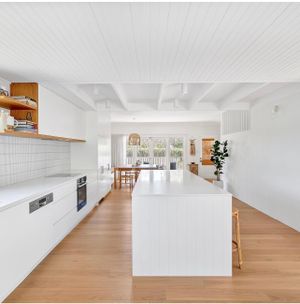 Bright white modern kitchen with long island, hardwood floors and pendant lighting.