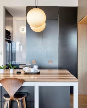 Contemporary kitchen corner with globe pendant lights, wooden counter and modern black cabinetry.