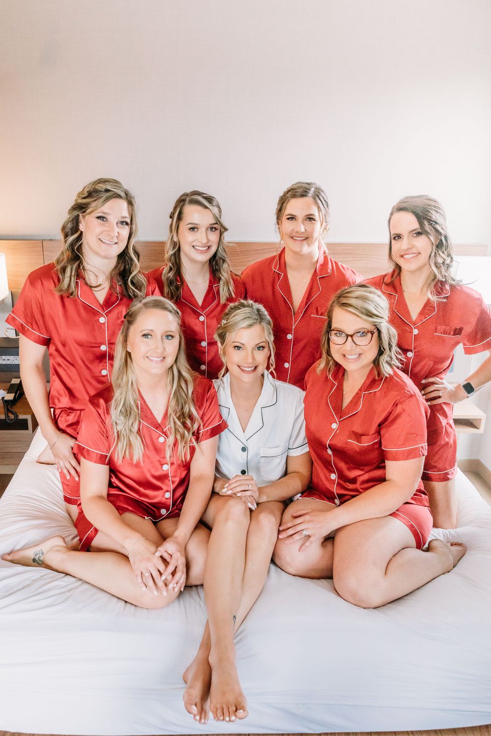Wedding party wearing matching red silk robes posing on white bed.