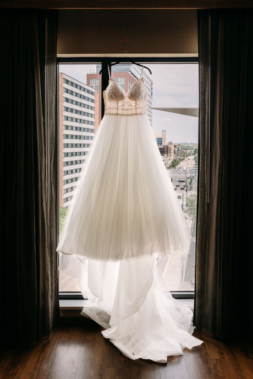 White wedding dress hanging in window frames with city view behind.