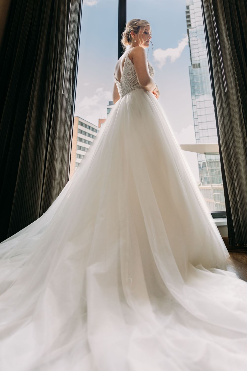 Elegant white wedding gown with flowing train captured in silhouette against city windows.