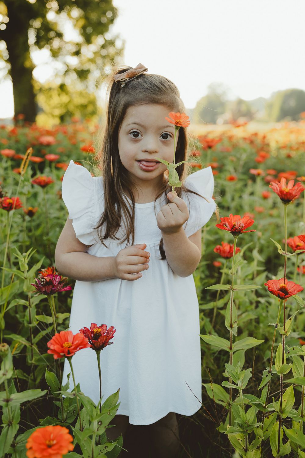 White-dressed figure holding orange flower amid garden of blooming poppies in warm sunlight.