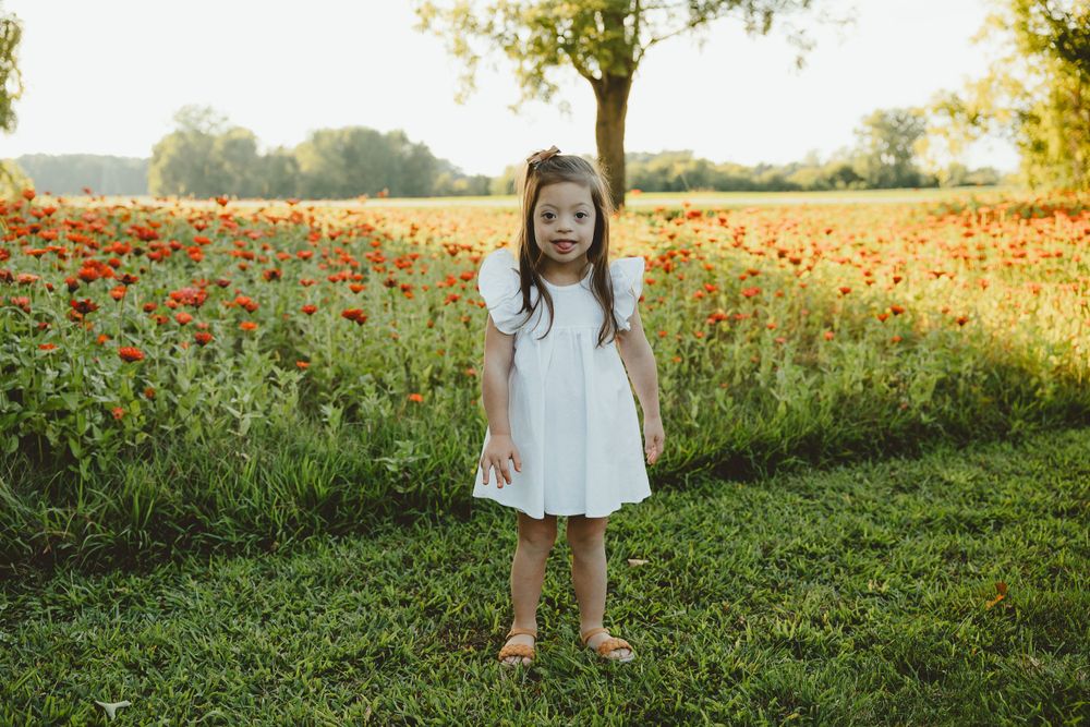 A white dress-clad figure stands in front of a vibrant field of orange poppies during golden hour.