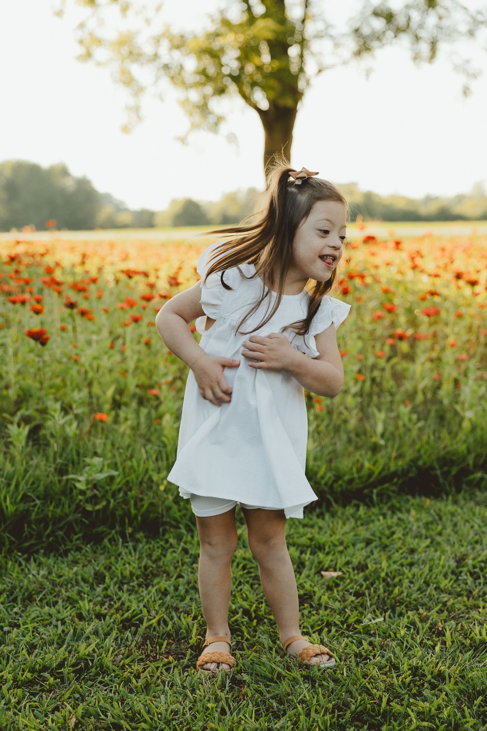 Figure in white dress laughing with joy while standing by field of orange poppies.