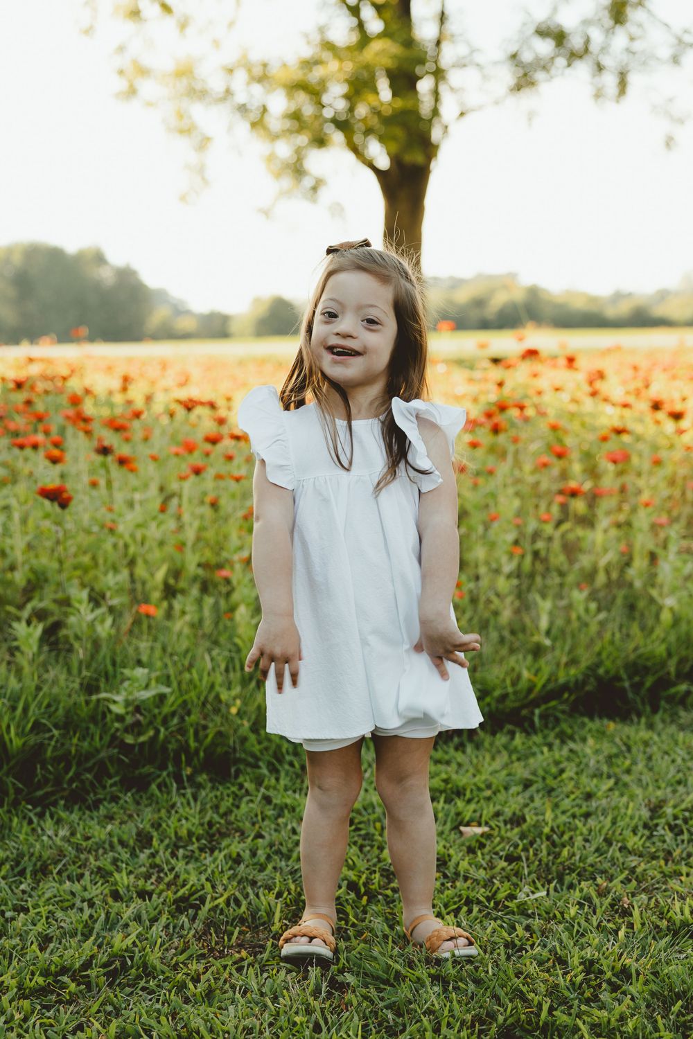 Figure stands cheerfully in white dress against backdrop of orange wildflowers.