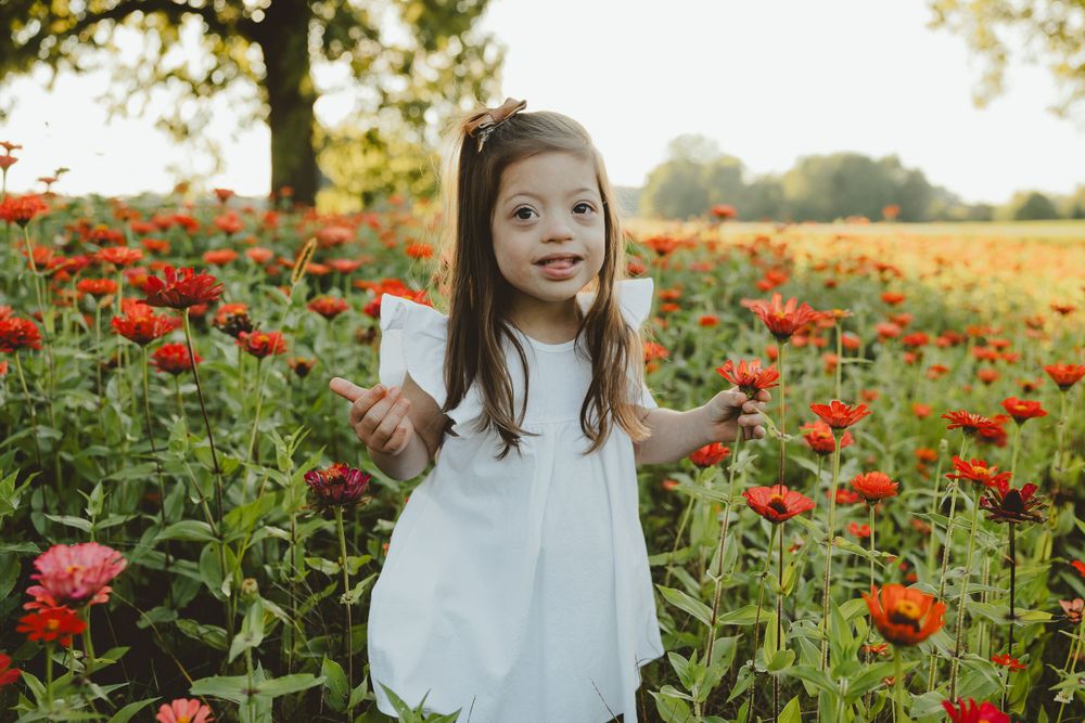 A joyful child wearing a white dress poses playfully in a field of vibrant red poppies during golden hour.