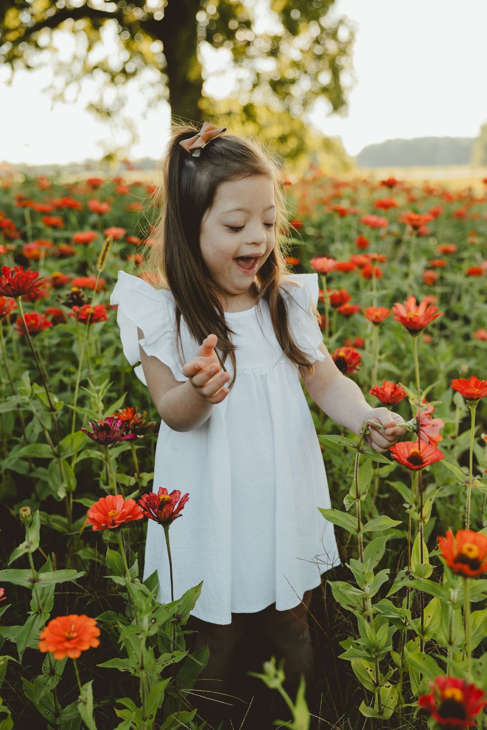 A child in a white dress laughs while exploring a blooming field of red poppies at sunset.