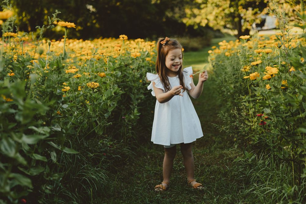 A child in a white dress dances joyfully among tall yellow wildflowers in late afternoon light.