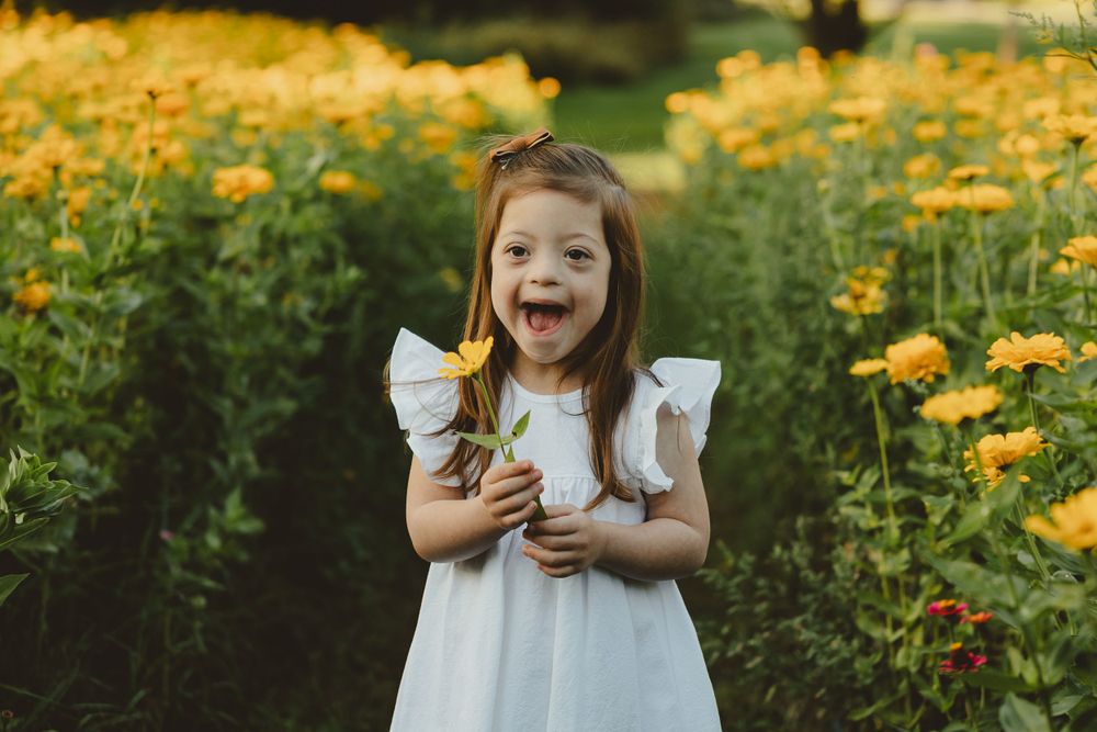 A gleeful child in a white dress laughs while standing in a field of golden summer flowers.