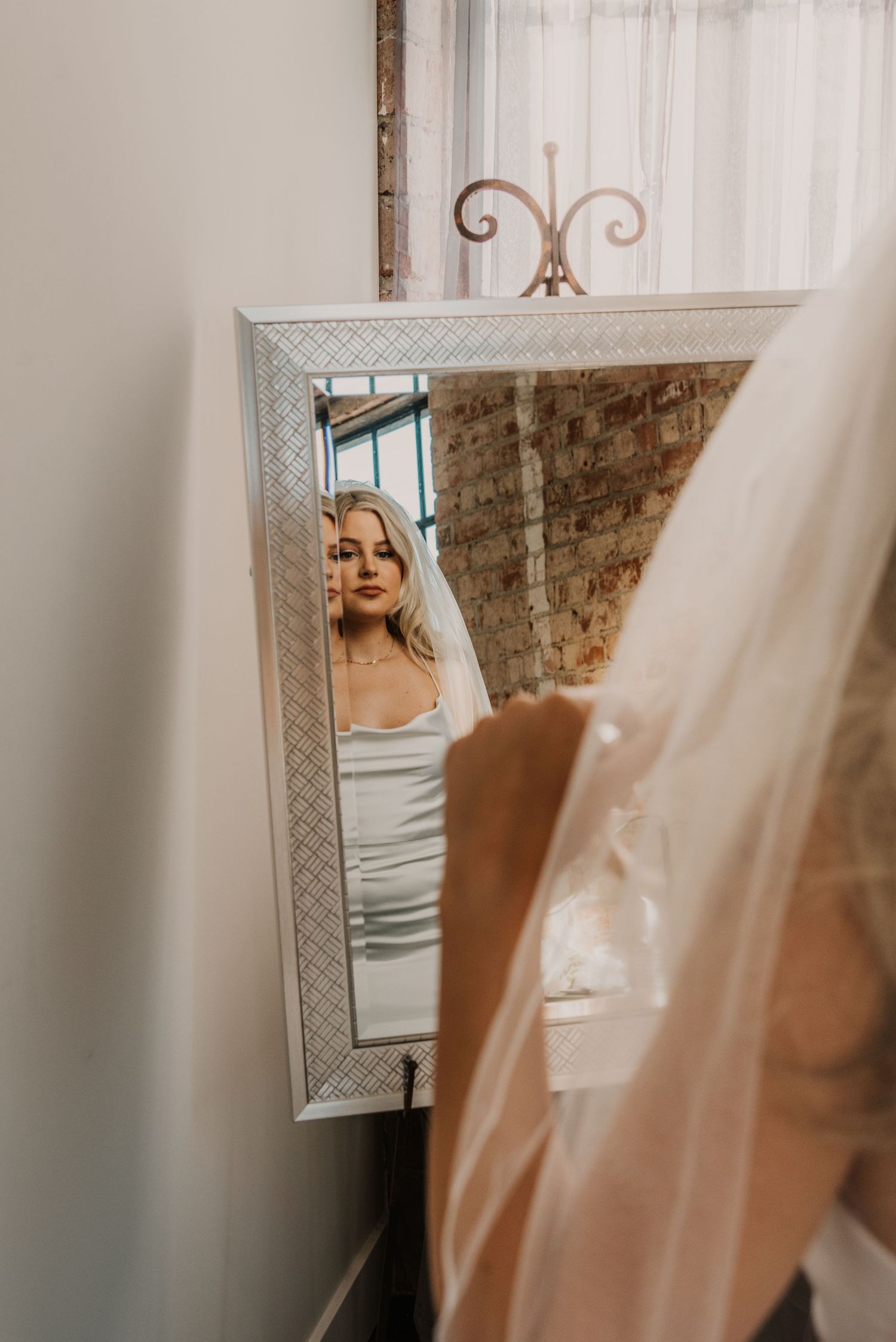 Wedding dress reflection seen in ornate mirror with soft natural lighting.