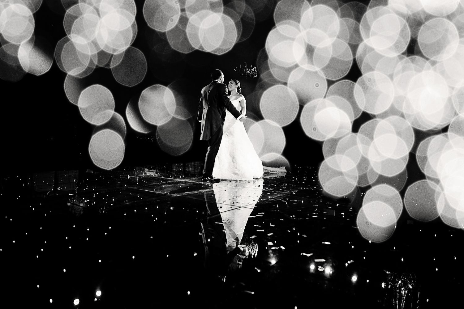 Black and white portrait at nighttime with bokeh lights reflecting on water.