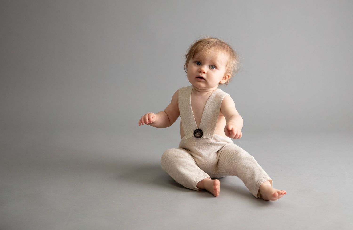 toddler sitter session, child wearing cream knitted homemade dungarees (up cycled from knitted dress) grey backdrop
