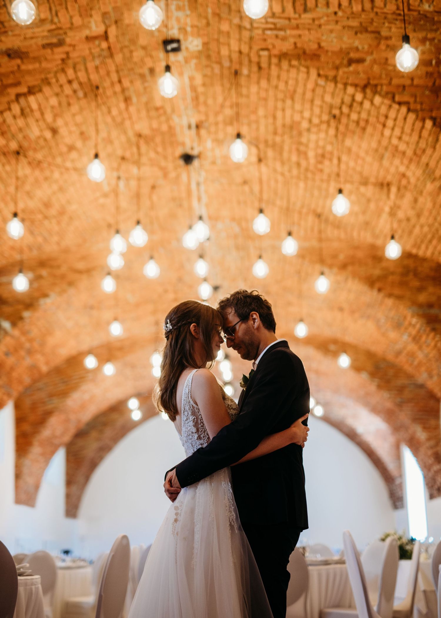 An intimate wedding moment under an arched brick ceiling with string lights.