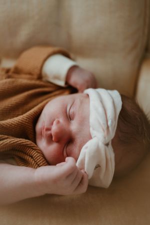 Close-up of sleeping newborn wearing white cap and brown clothing.