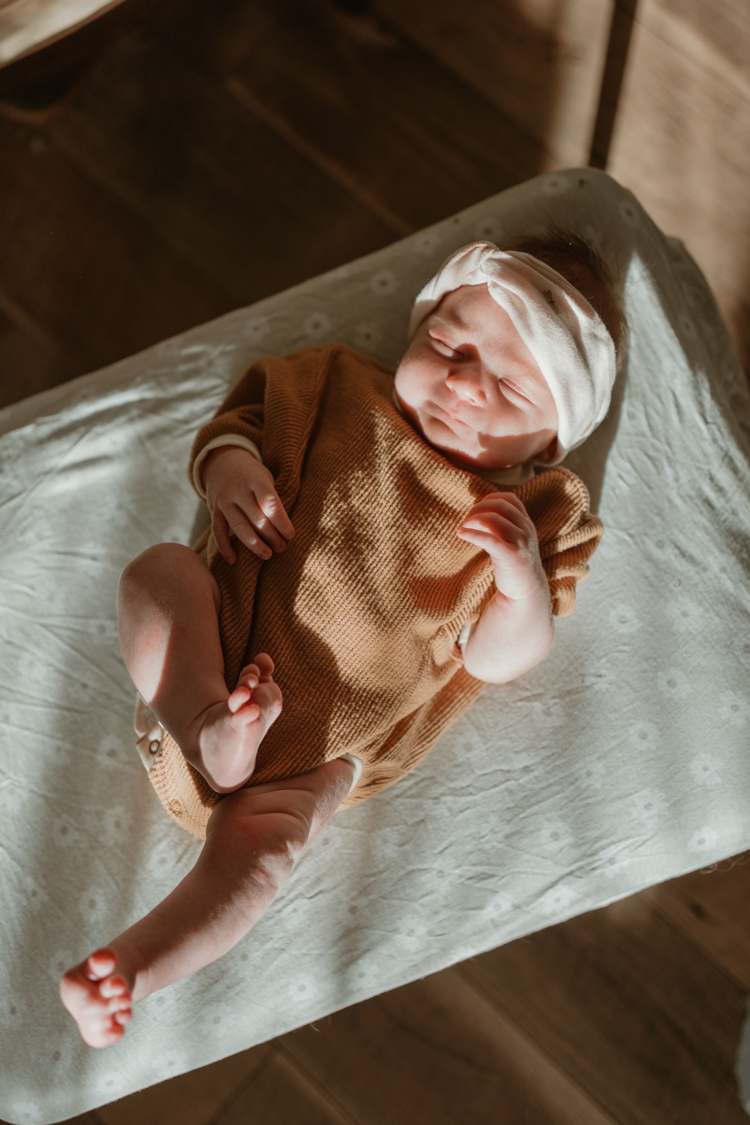 Sleeping newborn baby wearing knit outfit on white blanket.