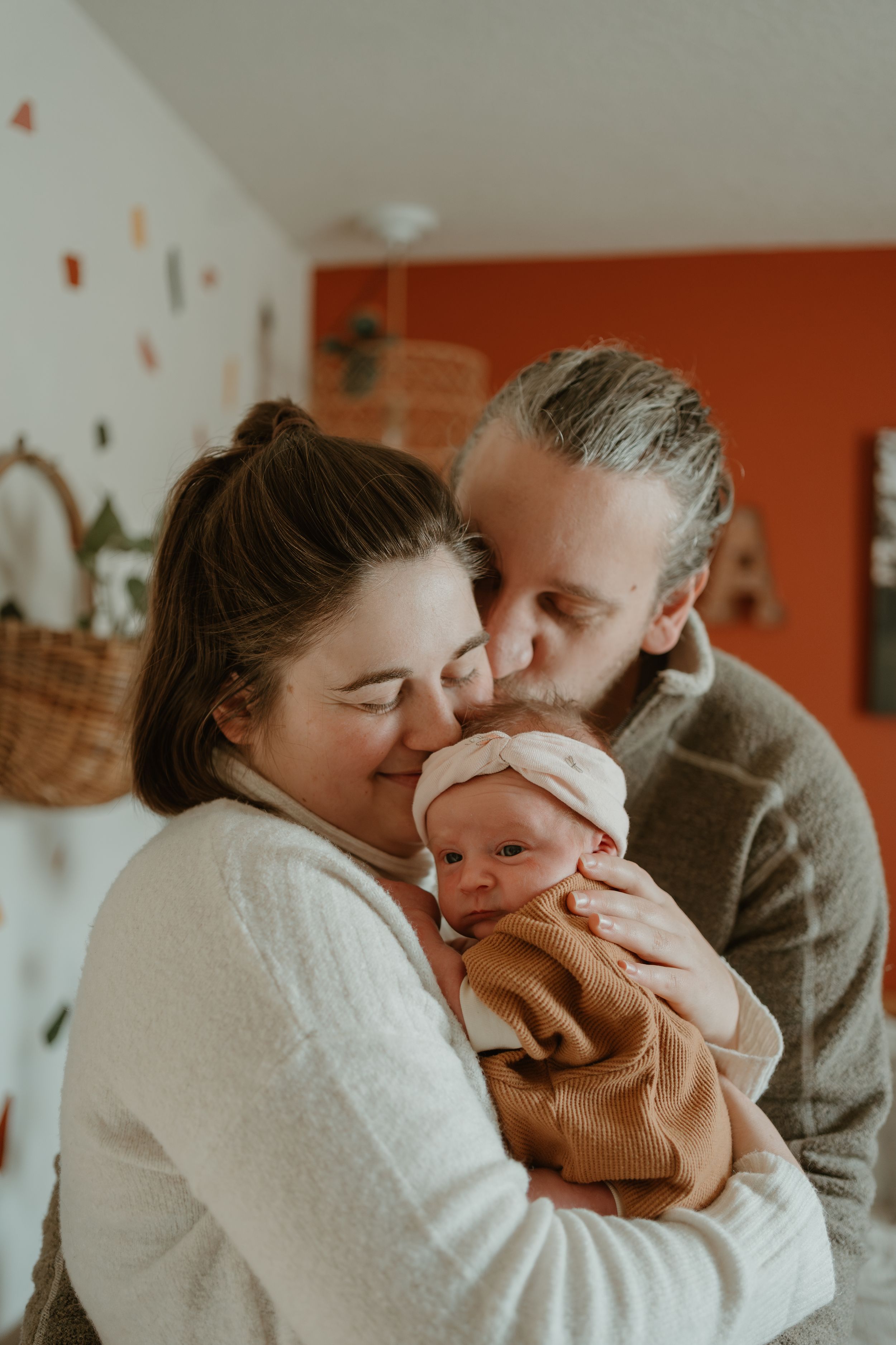 Intimate family moment with newborn baby wearing brown onesie being held and cuddled in warm lighting.