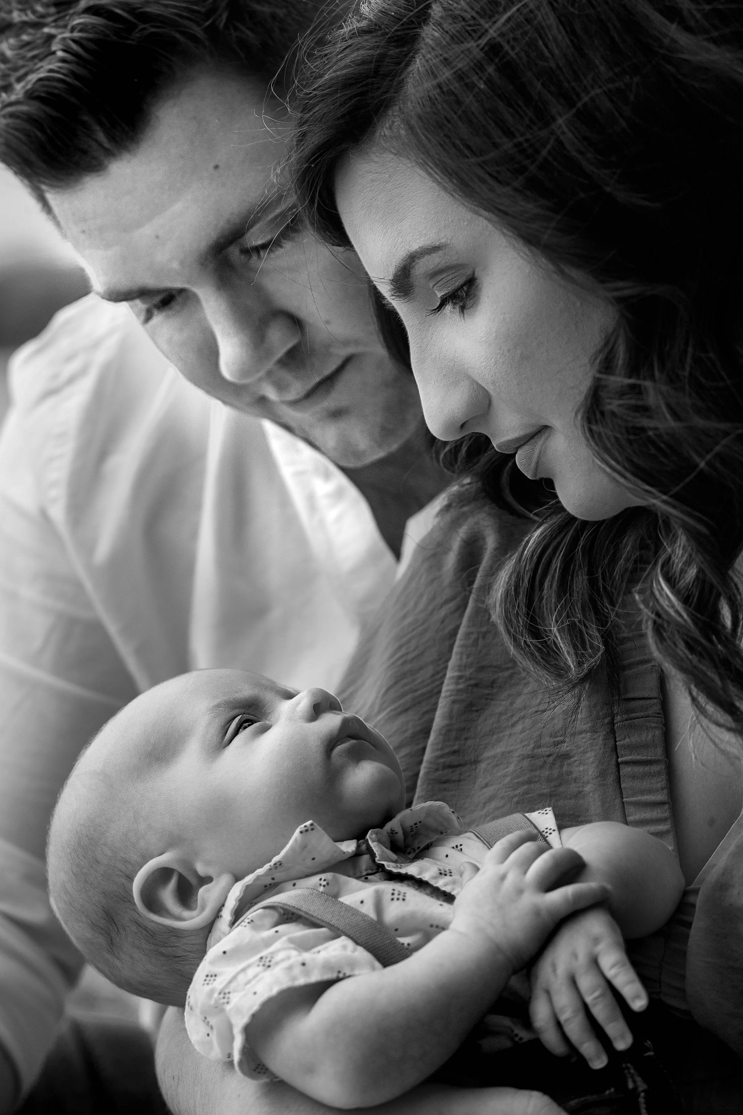 a black and white portrait of a mom and dad gazing down at their newborn son