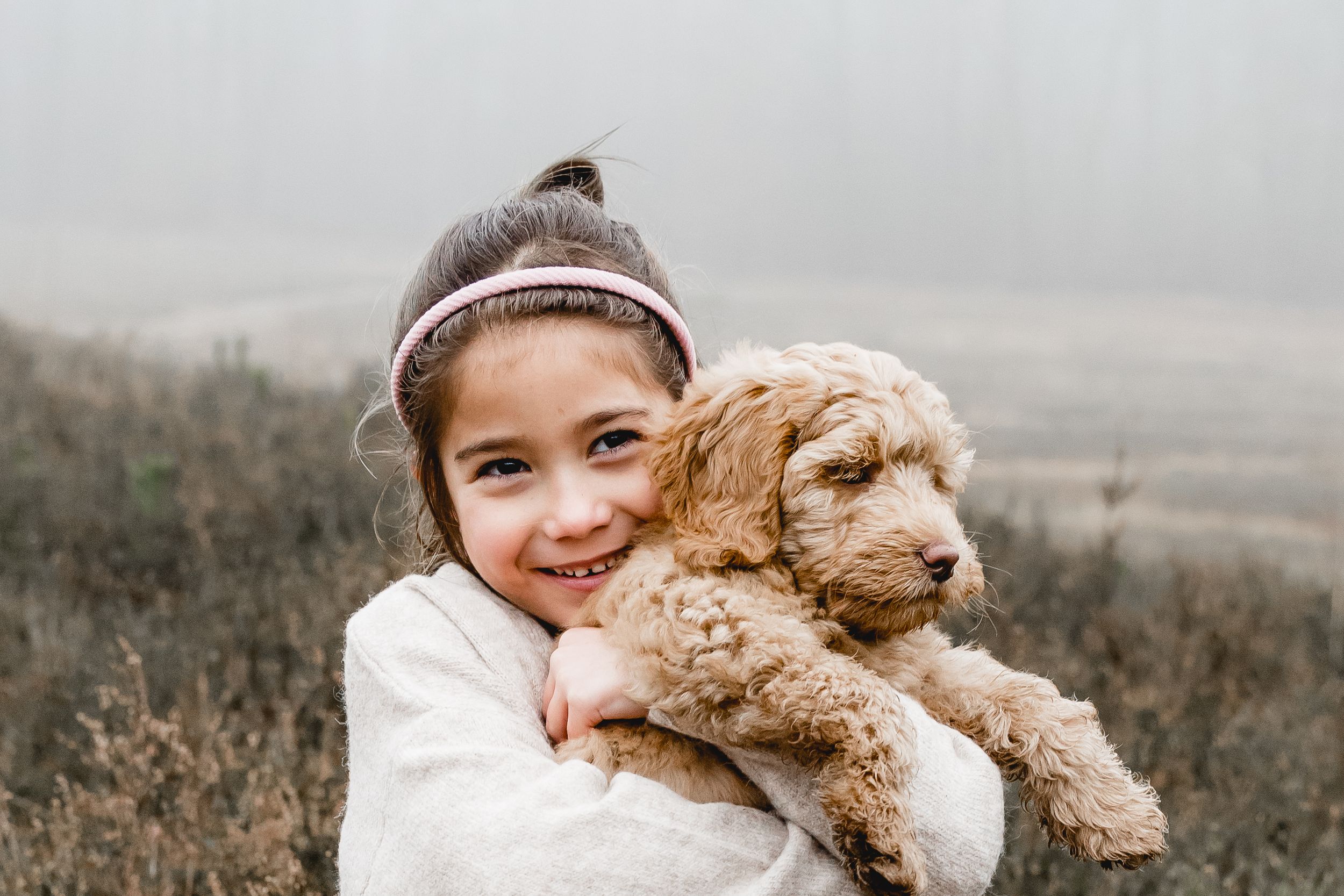 A teddy bear being hugged and cuddled outdoors on a misty day.