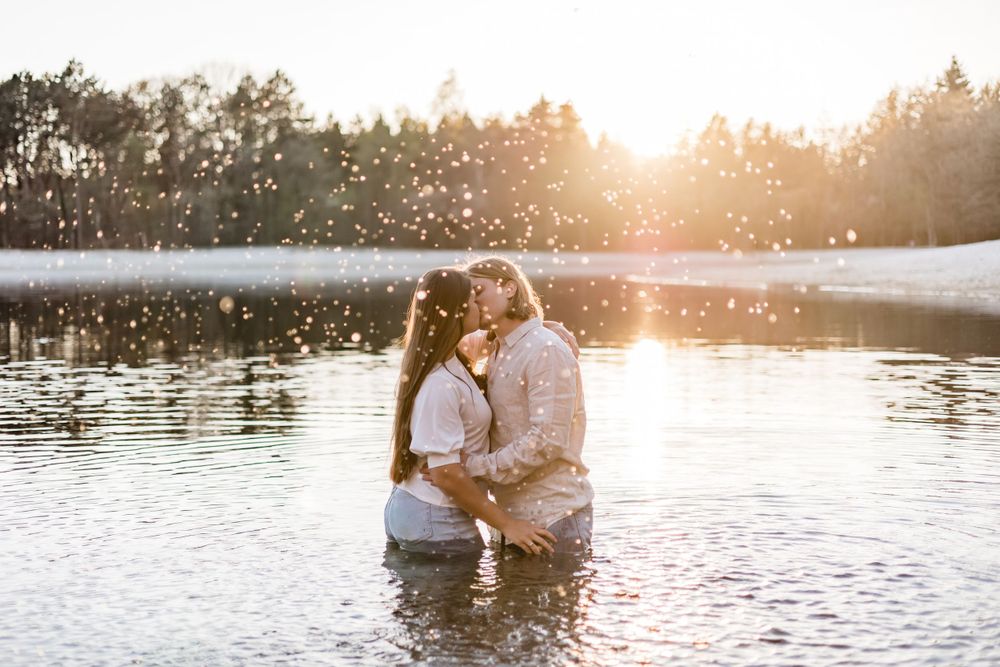 Romantic couple embracing in a lake at sunset with golden light reflecting on the water.