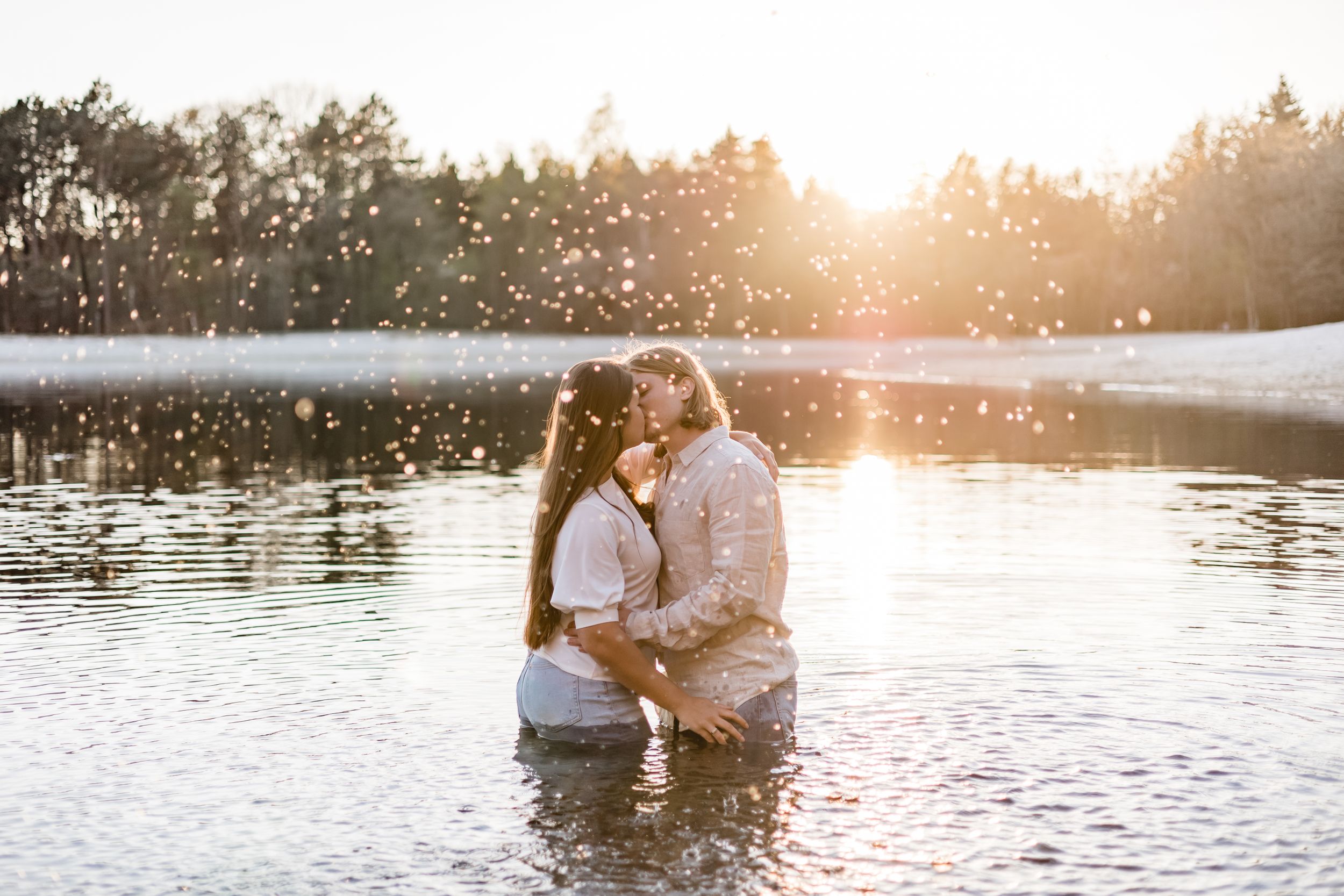 Romantic couple embracing in a lake at sunset with golden light reflecting on the water.