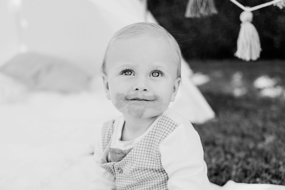 Black and white portrait of a young child in gingham clothing sitting in a garden setting.