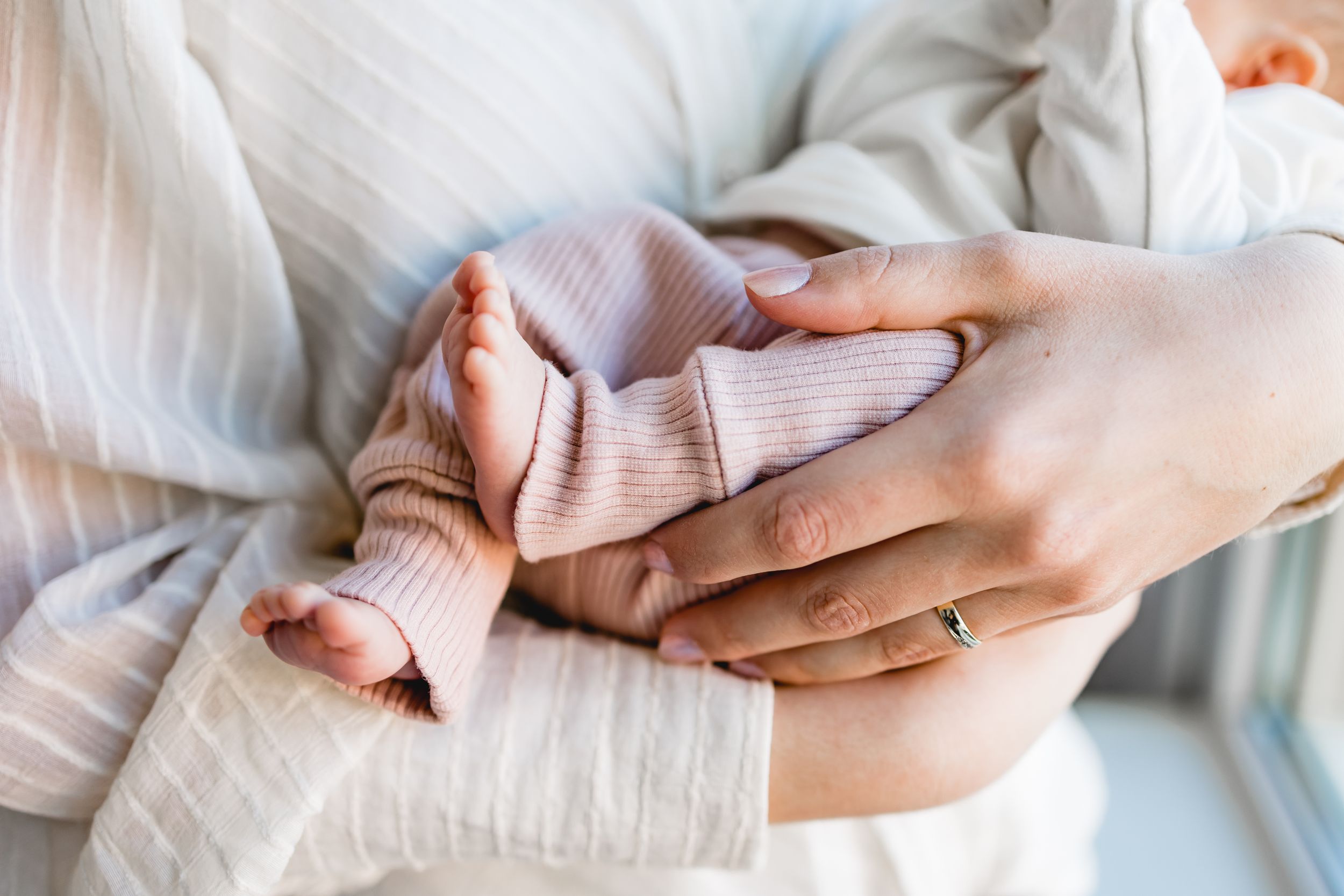 Close up of gentle hands holding and caressing a tiny newborn baby wrapped in soft white fabric.