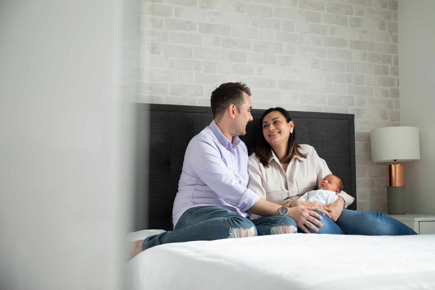 Intimate family moment at home with newborn in bright modern bedroom.