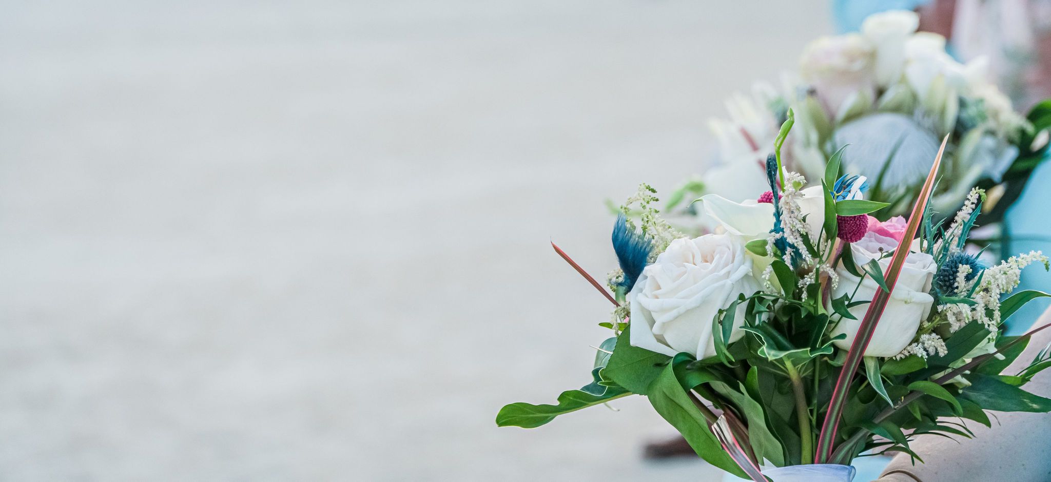 Beachfront wedding setup with white chairs and tropical floral arrangements.