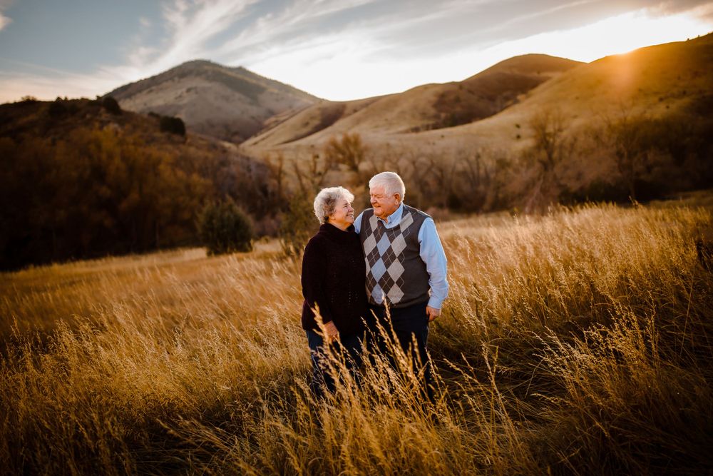 A couple smiles together in a golden grass field in Denver foot hills as the sun sets behind the mountains