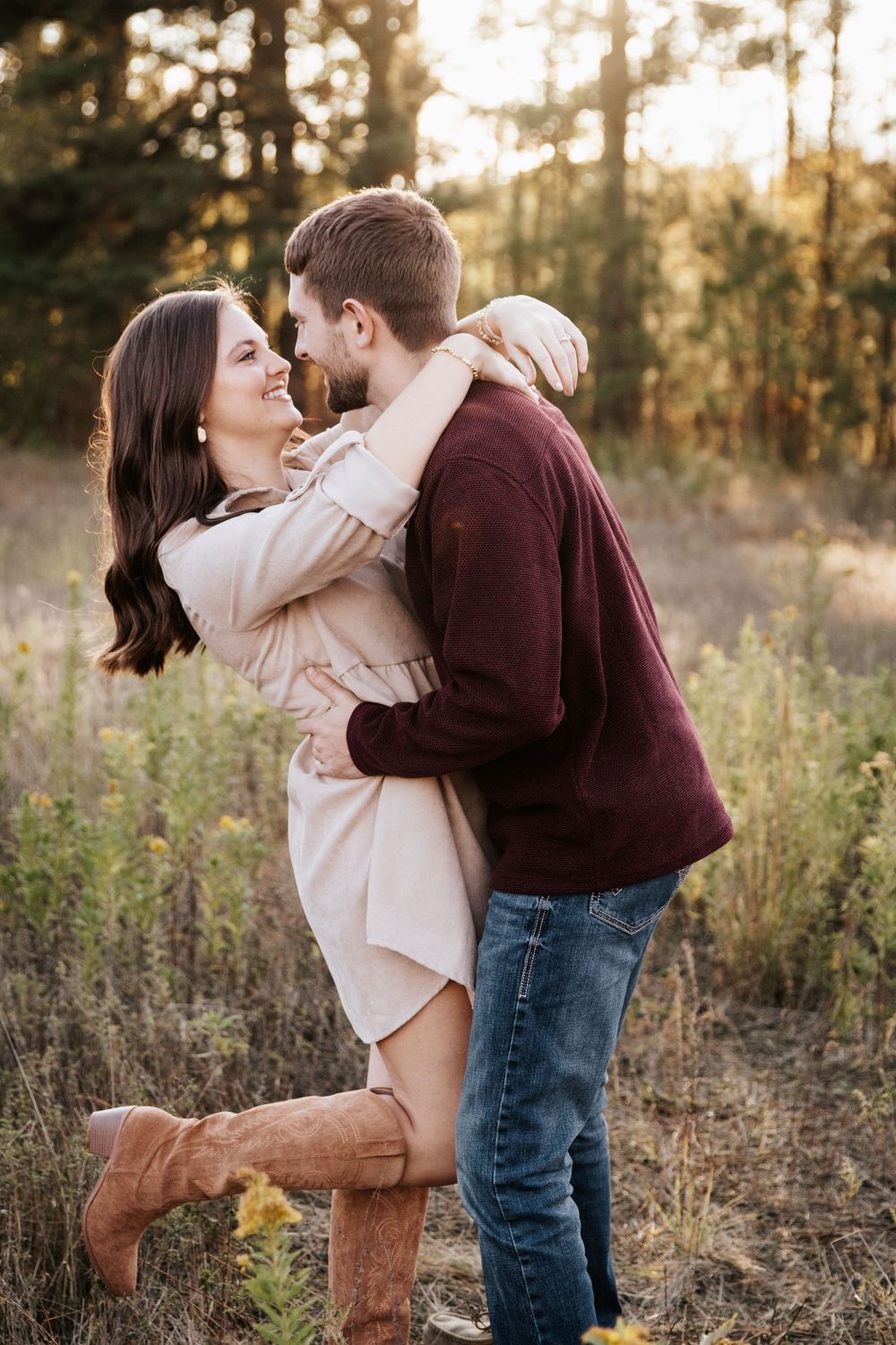 Romantic couple embracing in a field during golden hour wearing casual fall attire.