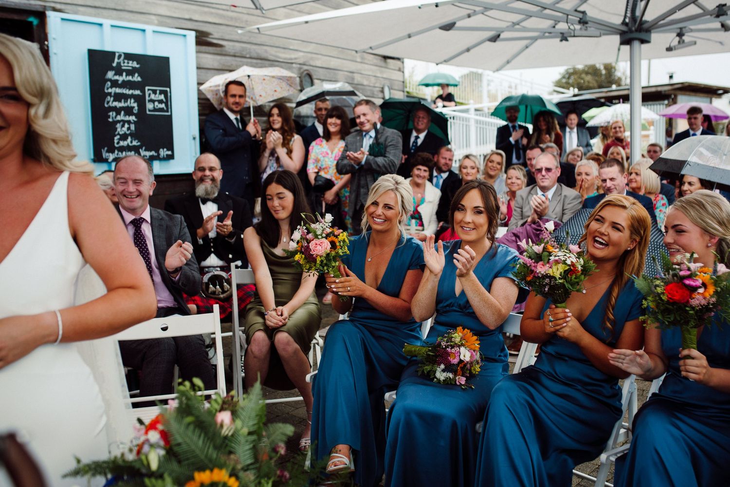 Wedding guests and bridesmaids in blue dresses watching ceremony outdoors.