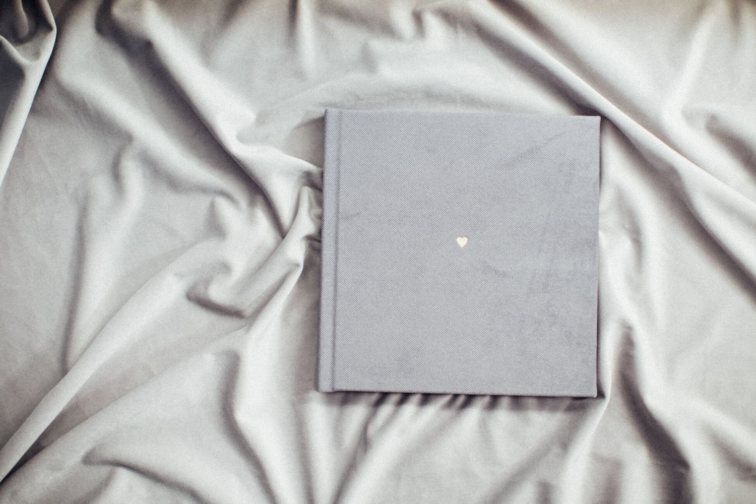 A minimalist gray photo album lying on soft fabric with subtle texture.