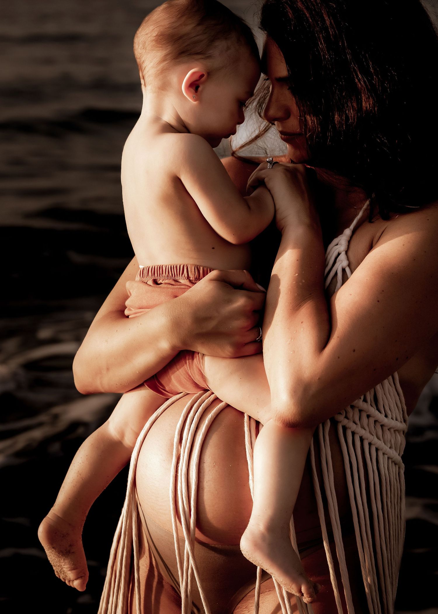 Mother and toddler baby girl embracing.  Beach at sunrise.  Sepia alternate editing process.