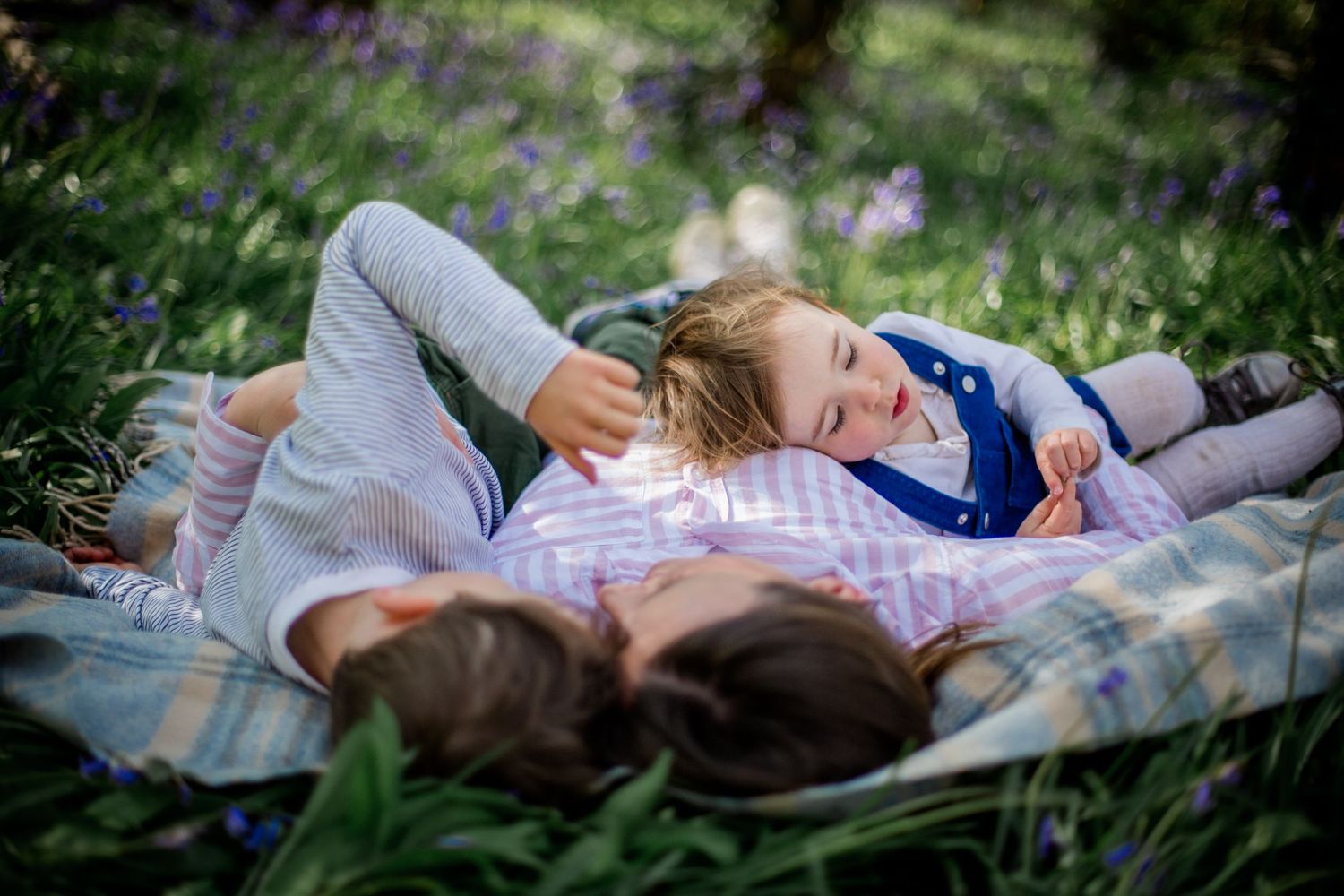 son, mother and daughter resting in the bluebells on a rug