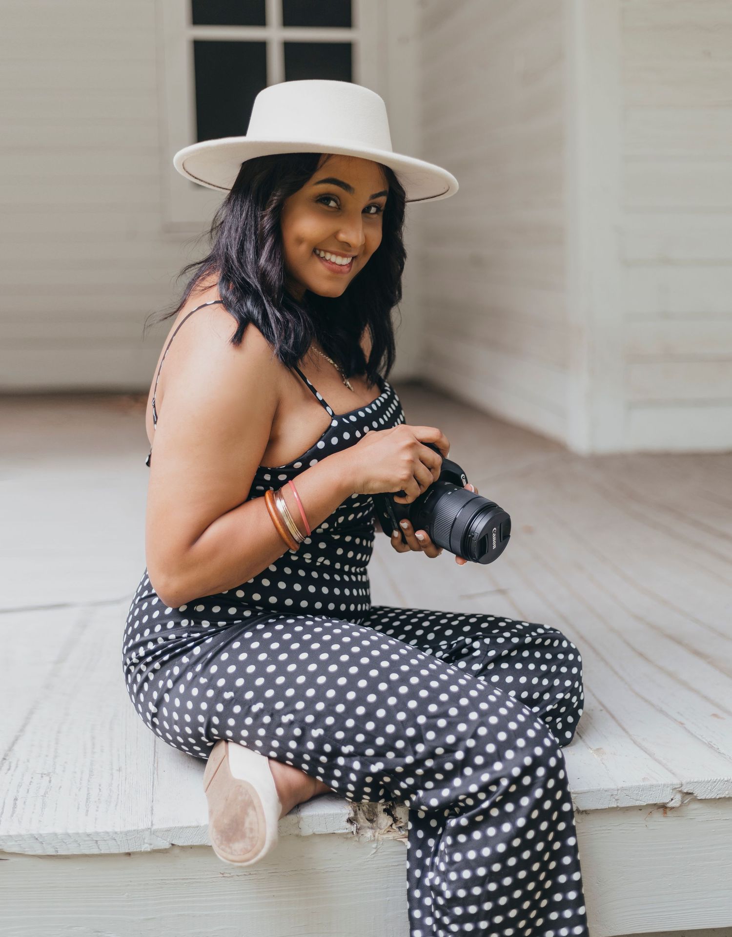 Photographer in polka dot dress with camera sits on white wooden floor.