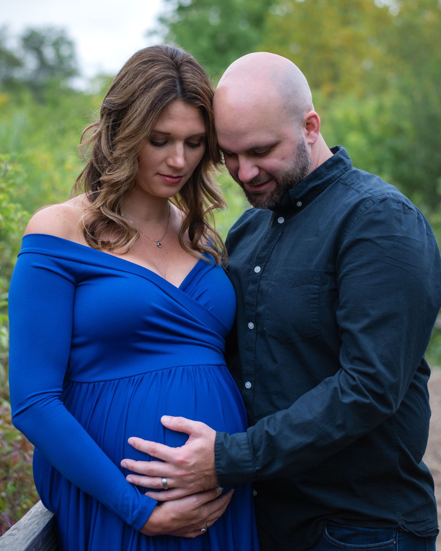 Intimate maternity photo of couple embracing outdoors in autumn with long blue dress and black shirt.