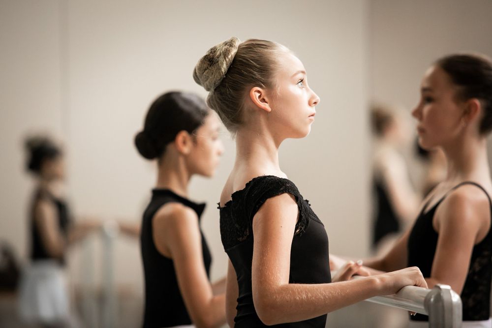 Ballet dancers in black leotards practicing in a dance studio.