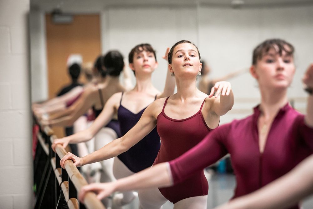 Ballet dancers practice at the barre in a dance studio during class.