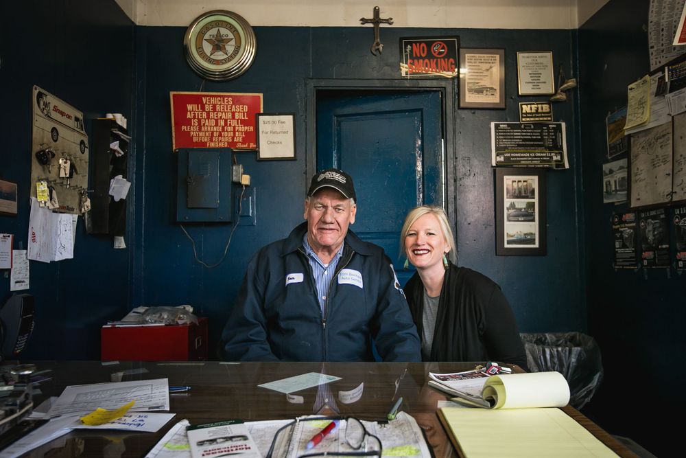 Two people sitting behind a desk in an office with blue walls covered in posters.