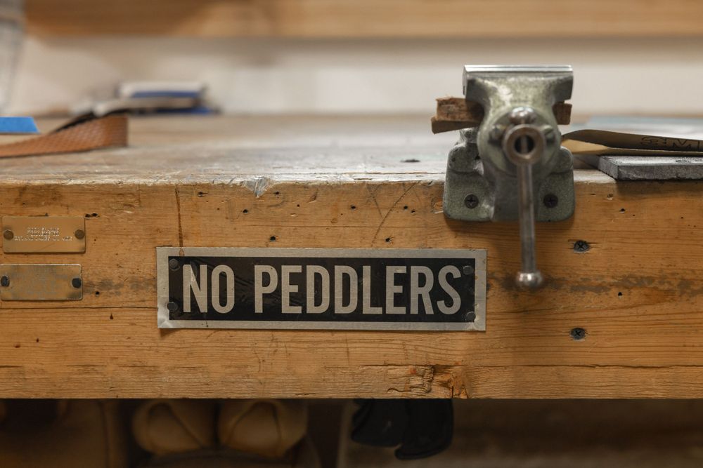 Wooden workbench with 'No Peddlers' sign and metal vise mounted on surface.