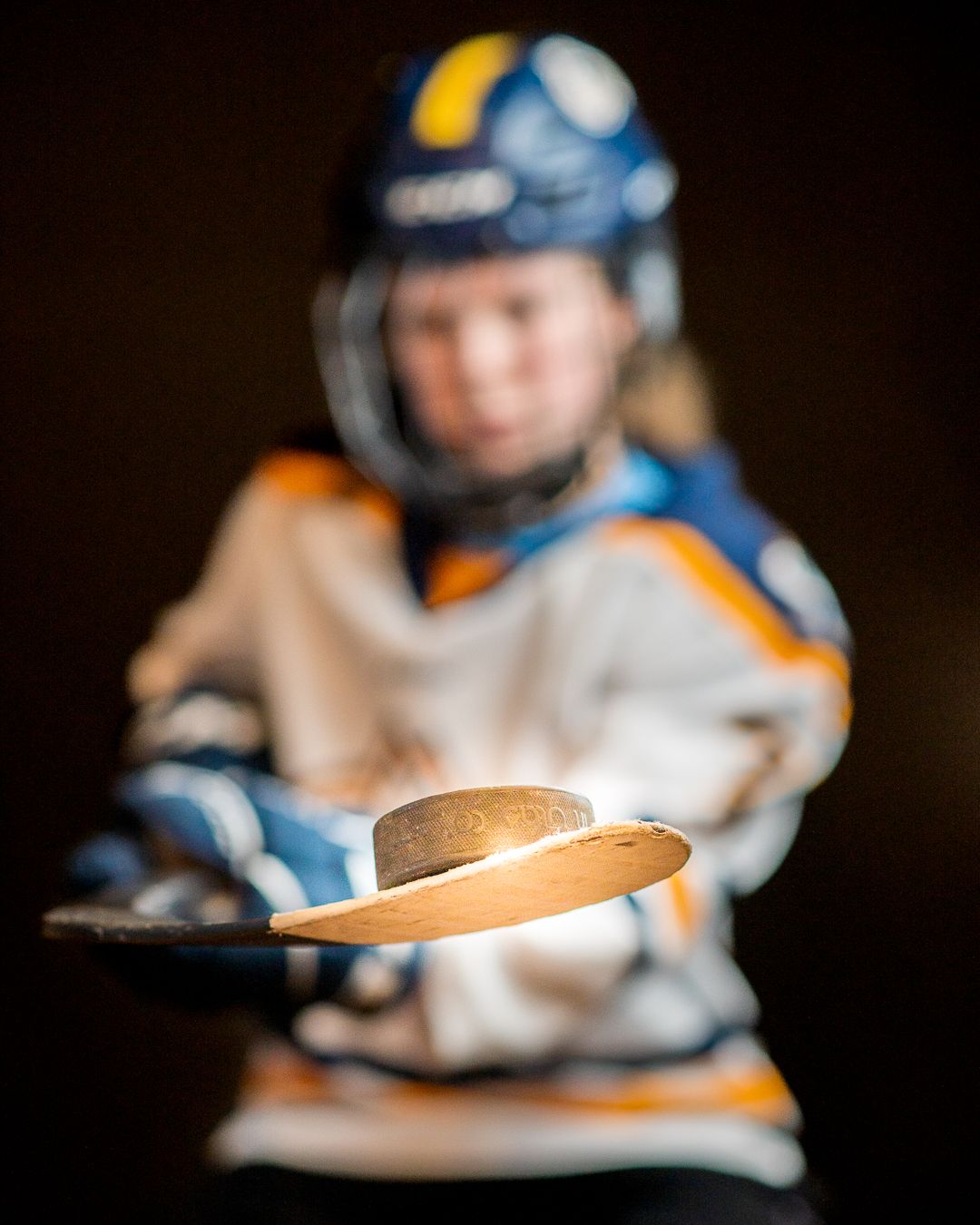 Hockey player in blue and orange jersey holding puck in focus with blurred background.