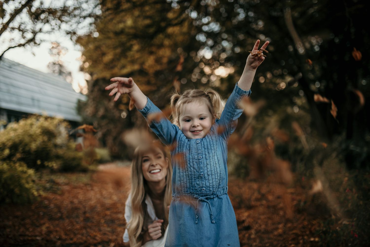 Children playing and raising arms joyfully in garden at sunset.