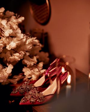 Elegant red sparkly wedding shoes displayed next to white flowers in warm lighting.